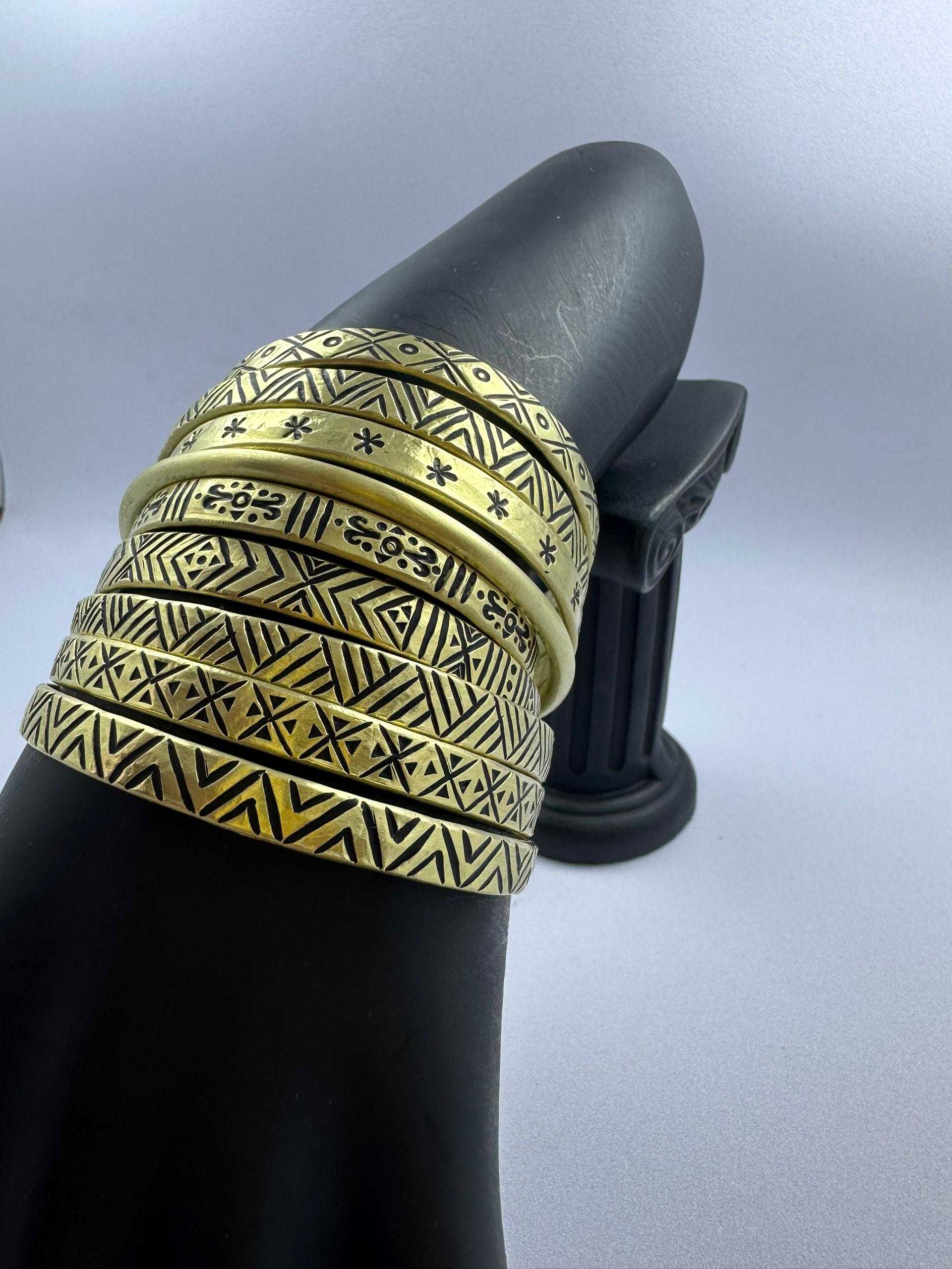 Stack of etched brass bracelets with geometric tribal patterns on a display stand